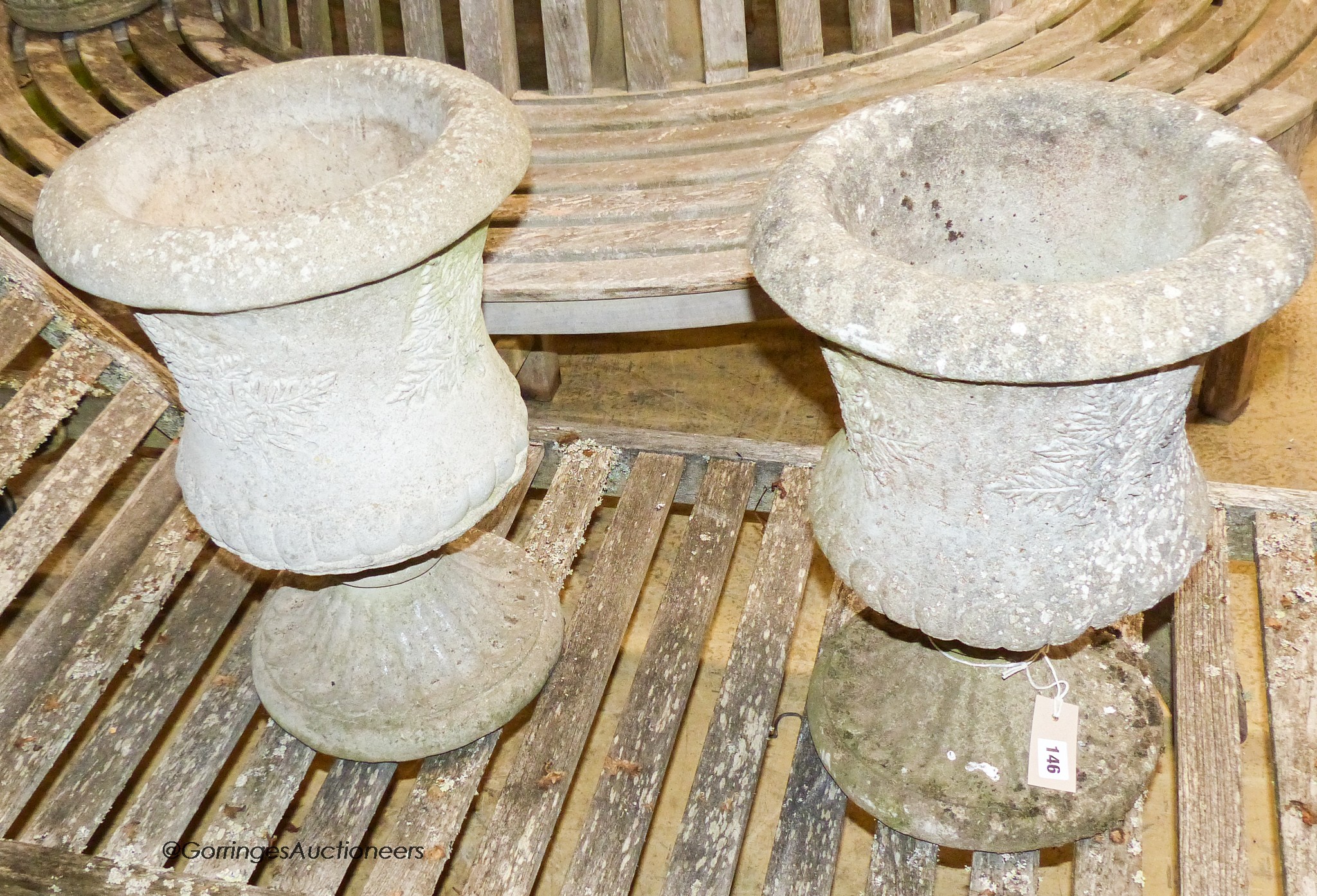 A pair of reconstituted stone campana-shaped urns on stands, decorated with ferns, diameter 34cm, height 49cm